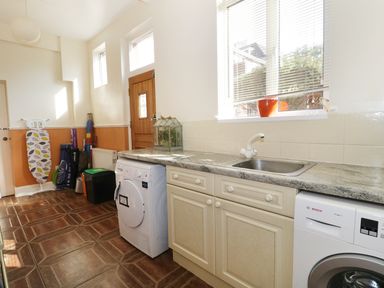 A utility room with a washing machine dryer sink ironing board and cleaning supplies at 20 Ulwell Road Swanage