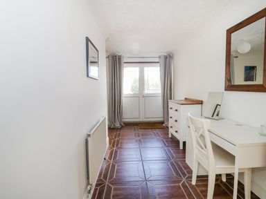 A hallway with tiled flooring a white radiator a white desk and chair a white chest of drawers and a door with curtains at 20 Ulwell Road Swanage