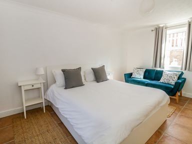 A bedroom with a bed white bedding and gray pillows beside two nightstands and a blue sofa by a window at 20 Ulwell Road in Swanage