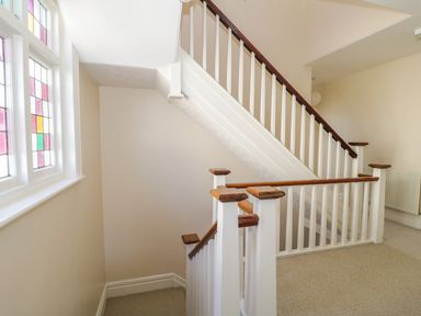A stairwell with white wooden banisters and brown handrails next to a window with colored glass panels at 20 Ulwell Road in Swanage