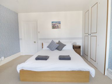 A bedroom with a wooden bed with white bedding and two gray towels a bedside table and a closed wardrobe at 20 Ulwell Road in Swanage