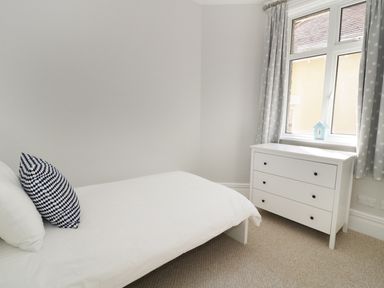 A small bedroom with a bed a pillow a chest of drawers and a window with curtains at 20 Ulwell Road in Swanage