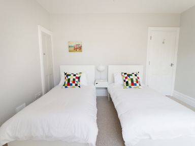 A bedroom with two single beds each with a colorful checkered pillow and a small white nightstand with a lamp between them at 20 Ulwell Road Swanage