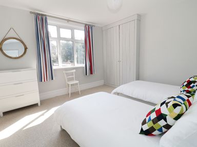 A bedroom with two beds colorful pillows a white chair a white dresser a circular mirror striped curtains and a built-in wardrobe at 20 Ulwell Road in Swanage