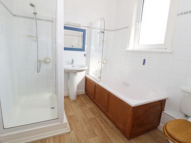 A bathroom with a shower enclosure sink bathtub with wooden panel and a toilet with a wooden seat at 20 Ulwell Road in Swanage