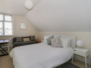A bedroom with a bed with pillows a small side table with a lamp a sofa with cushions and a desk with a chair at 20 Ulwell Road in Swanage