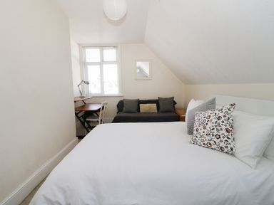 A bedroom with a bed and pillows a sofa and a desk near the window at 20 Ulwell Road in Swanage