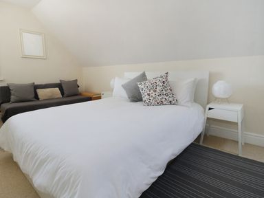 A bedroom with a white bed and pillows next to a gray sofa with cushions at 20 Ulwell Road in Swanage