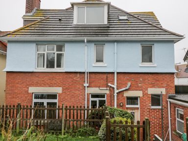 A two story house with blue and red brick exterior a wooden fence and shrubbery at 20 Ulwell Road Swanage