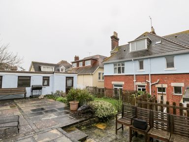A backyard with patio furniture a barbecue and plants next to houses at 20 Ulwell Road in Swanage