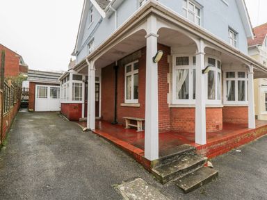 The exterior of a house with a covered porch supported by white columns and a driveway leading to a garage at 20 Ulwell Road in Swanage