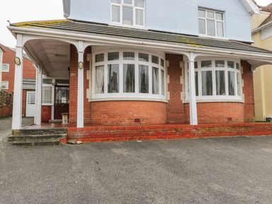 The front view of a two-story house with a tiled roof two large bay windows and a covered porch area at 20 Ulwell Road in Swanage