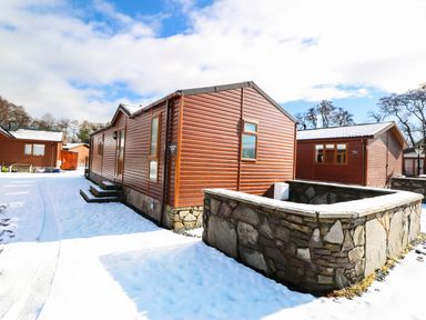 A wooden cabin with stone foundation surrounded by snow at 32 Cruachan Lodge in Auchterarder