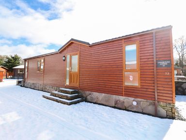 A wooden lodge with steps leading to a door surrounded by snow at 32 Cruachan Lodge in Auchterarder