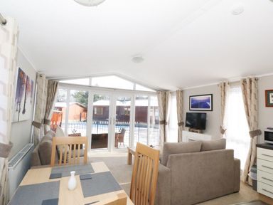 A living room with sofas a dining table with chairs and large glass doors at 32 Cruachan Lodge in Auchterarder