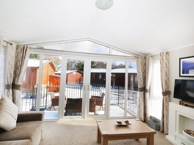 A living room with sofa coffee table TV and large glass doors leading to a patio at 32 Cruachan Lodge in Auchterarder