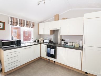 A kitchen with white cabinets a microwave oven a toaster kettle and a window with striped blinds at 32 Cruachan Lodge in Auchterarder