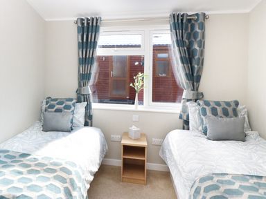 A bedroom with two single beds and patterned curtains at 32 Cruachan Lodge in Auchterarder