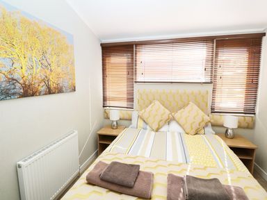 A bedroom with a double bed and bedside tables with lamps and a large window with blinds at 32 Cruachan Lodge in Auchterarder