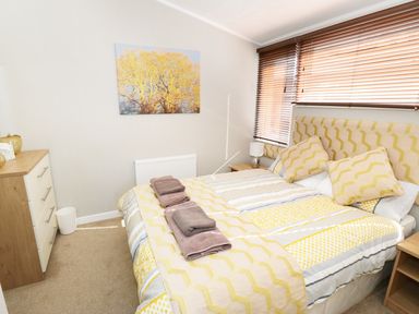 A bedroom with a double bed with yellow patterned bedding two bedside tables with lamps a chest of drawers and a wall picture at 32 Cruachan Lodge in Auchterarder