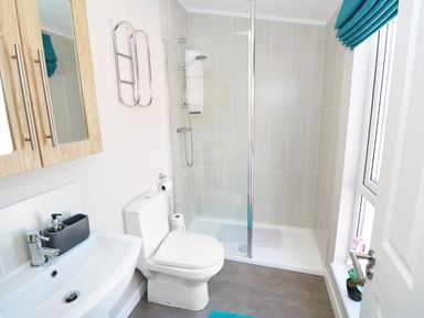 A bathroom with a white toilet sink wooden cabinet glass shower and window at 32 Cruachan Lodge in Auchterarder
