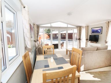 A dining table with wooden chairs and a vase in a room with sofas and a tv at 32 Cruachan Lodge in Auchterarder