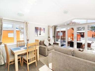 A dining area with a wooden table and chairs next to a living room with sofas and large windows at 32 Cruachan Lodge in Auchterarder