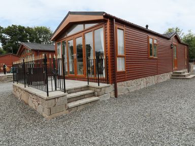 A brown wooden lodge with a stone base and small steps leading to a fenced patio at 32 Cruachan Lodge in Auchterarder