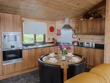 A kitchen with wooden cabinets and a round table at The Cabin at East Hill Pride Four Elms Hill Nr. Sidmouth
