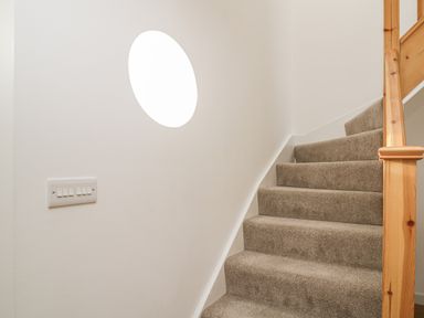 A carpeted staircase with a wooden handrail and a round window on the wall at Coney Garth Barn in Beckermet