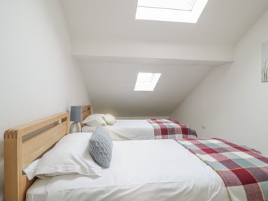 A bedroom with two single beds, pillows, checked blankets, and skylights at Coney Garth Barn in Beckermet