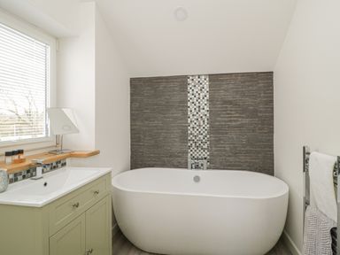 A bathroom with a freestanding bathtub a sink with vanity and towels on a rack at Coney Garth Barn in Beckermet