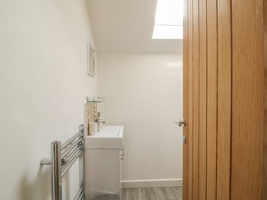 A small bathroom with a wooden door a sink with soap dispensers a towel radiator and a skylight at Coney Garth Barn in Beckermet
