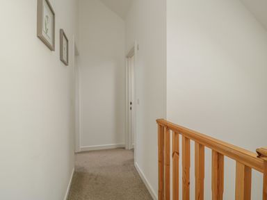 A hallway with beige carpet two doorways and wooden banister at Coney Garth Barn in Beckermet