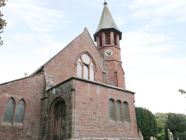 The exterior of a stone church with a clock tower and arched windows surrounded by trees