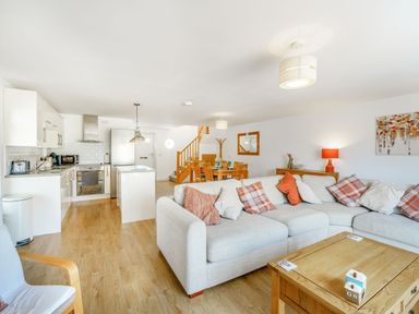 An open-plan living area with a beige sectional sofa and wooden coffee table next to a kitchen with white cabinets and stainless appliances at Coney Garth Barn in Beckermet