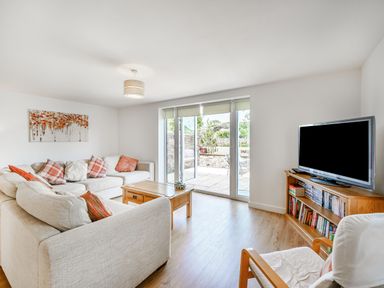 A living room with a beige sectional sofa and wooden coffee table near glass doors and a TV on a wooden stand at Coney Garth Barn in Beckermet