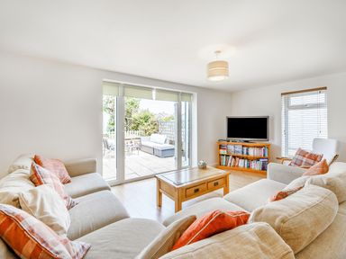 A living room with sofas a wooden coffee table a TV on a wooden stand and glass doors leading to a patio at Coney Garth Barn in Beckermet
