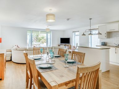 An open plan dining and living room with wooden dining table and chairs and a kitchen with white cabinets at Coney Garth Barn in Beckermet