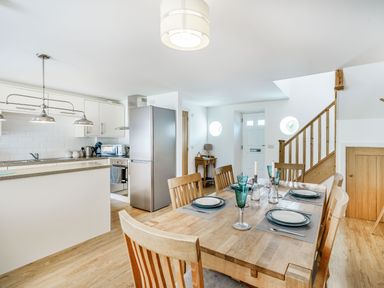 A kitchen and dining area with wooden table and chairs a refrigerator and stairs at Coney Garth Barn in Beckermet