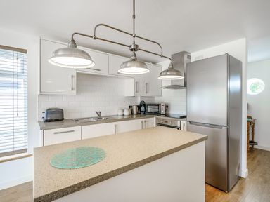 A kitchen with white cabinets stainless steel appliances pendant lights and a countertop at Coney Garth Barn in Beckermet