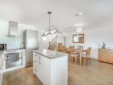 A kitchen and dining area with an island, stainless steel fridge, wooden dining table with chairs, and wooden floor at Coney Garth Barn in Beckermet