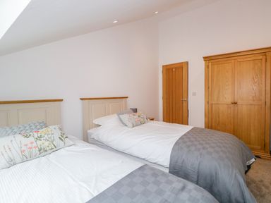 A bedroom with two single beds a wooden wardrobe and a wooden door at Coney Garth Cottage in Beckermet