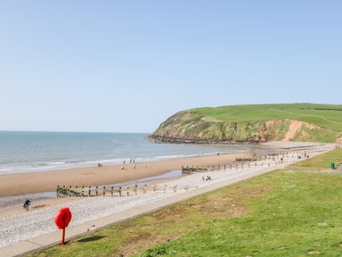 A sandy beach with people walking and a green hill in the background at Coney Garth Cottage in Beckermet