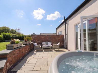 An outdoor area with a hot tub and seating at Coney Garth Cottage in Beckermet