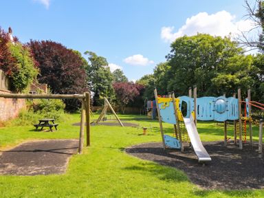 A playground with swings and a slide in an outdoor area at Coney Garth Cottage Beckermet