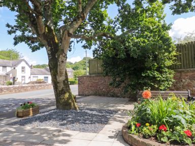 An outdoor area with a tree, bench, and flower bed at Coney Garth Cottage in Beckermet