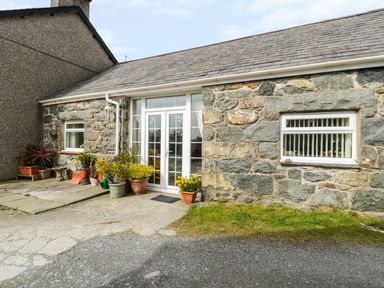 Stone exterior of a house with white framed glass double doors and potted plants on the paved area at Bwthyn Ael Y Bryn in Criccieth