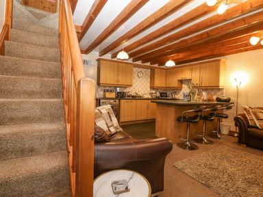 A living area with a staircase a kitchen island with bar stools and leather sofas at Bwthyn Ael Y Bryn in Criccieth