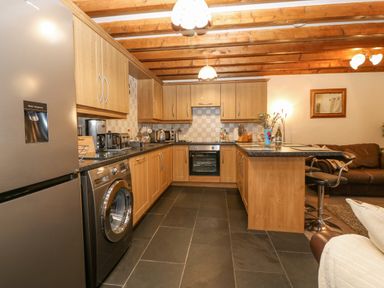 A kitchen with wooden cabinets black appliances and a seating area at Bwthyn Ael Y Bryn in Criccieth
